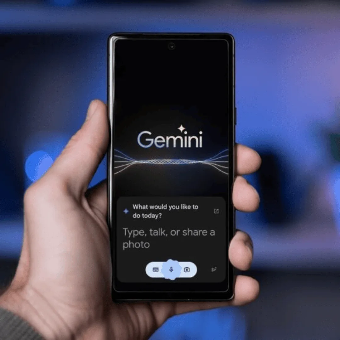 Hand holding phone displaying Gemini app with prompt to type, talk, or share a photo.